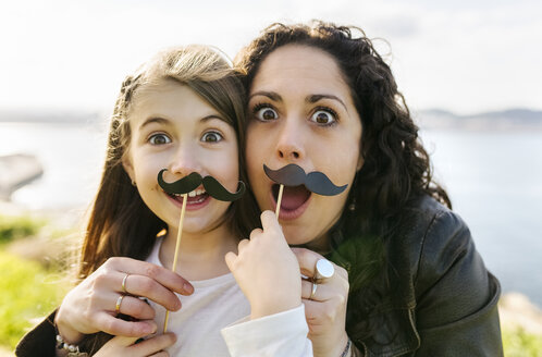 Mother and daughter having fun holding fake moustaches - MGOF03232