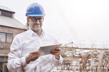 Portrait of smiling man with tablet wearing blue hart hat - FMKF03865