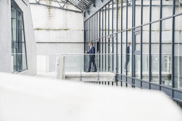 Businessman walking on skywalk looking at cell phone - FMKF03881