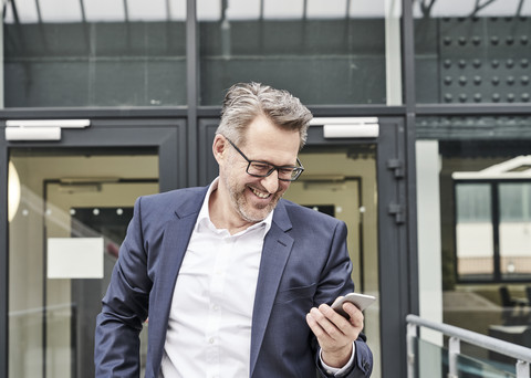 Lachender Geschäftsmann mit Blick auf sein Handy, lizenzfreies Stockfoto