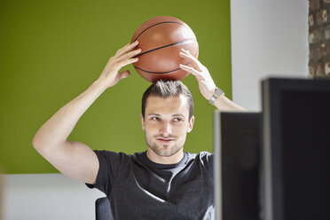 Young man working in office, balancing a basketball - RHF01905