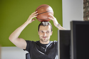Junger Mann arbeitet im Büro und balanciert einen Basketball - RHF01905