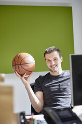 Young man working in office, balancing a basketball - RHF01906