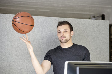 Junger Mann arbeitet im Büro und balanciert einen Basketball - RHF01907