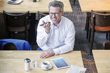 Glücklicher reifer Geschäftsmann in einem Café, der ein Mobiltelefon benutzt - FMKF03916