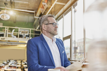 Mature businessman in cafe with newspaper looking sideways - FMKF03929