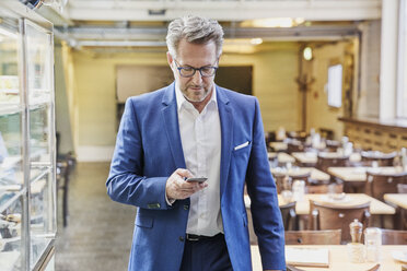 Älterer Geschäftsmann im Café schaut auf sein Handy - FMKF03931