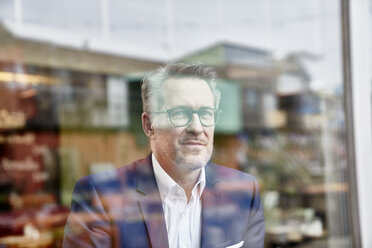 Portrait of confident mature businessman behind windowpane - FMKF03934