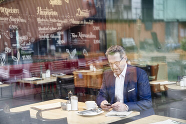 Reifer Geschäftsmann in einem Café, der ein Mobiltelefon benutzt - FMKF03936