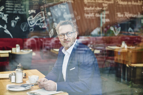 Reifer Geschäftsmann in einem Café, der ein Mobiltelefon benutzt - FMKF03937