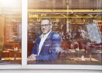 Confident mature businessman looking out of window - FMKF03945