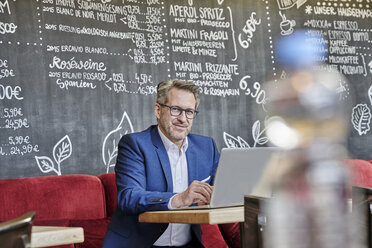 Porträt eines selbstbewussten reifen Geschäftsmannes in einem Café mit Laptop - FMKF03951