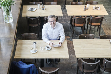 Lächelnder reifer Geschäftsmann im Café mit Tablet - FMKF03954