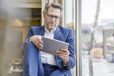 Reifer Geschäftsmann mit Tablet am Fenster - FMKF03962