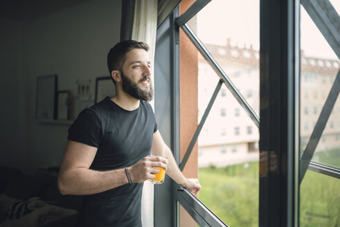 Junger Mann trinkt einen Orangensaft am Fenster - RAEF01830