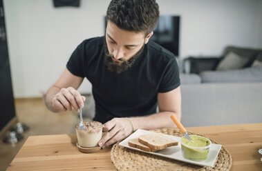 Junger Mann bereitet sein Frühstück zu Hause vor, indem er Kakao und Milch mischt - RAEF01835