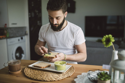 Junger Mann beim Frühstück zu Hause, Toast mit Avocadocreme, lizenzfreies Stockfoto