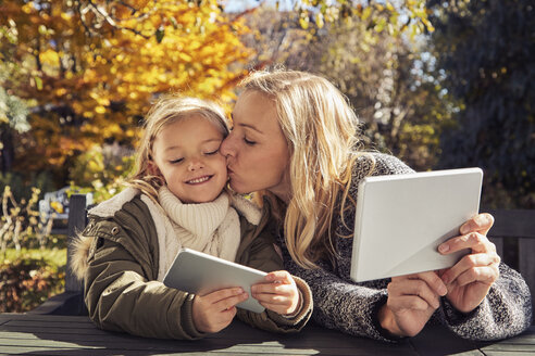 Mother with daughter at garden table holding tablet and cell phone - KDF00726