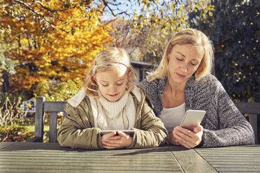 Mother with daughter at garden table using cell phones - KDF00727
