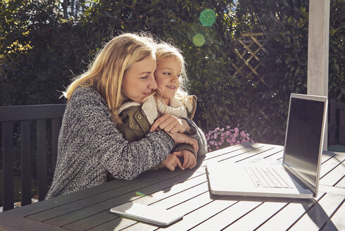 Mutter mit Tochter am Gartentisch mit Blick auf den Laptop - KDF00729