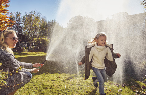 Mother and daughter playing with garden hose in autumn stock photo