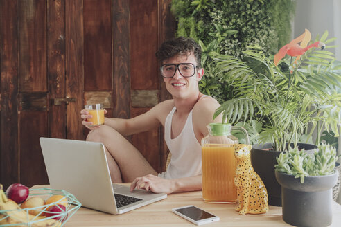 Young man using laptop and drinking orange juice at home - RTBF00826