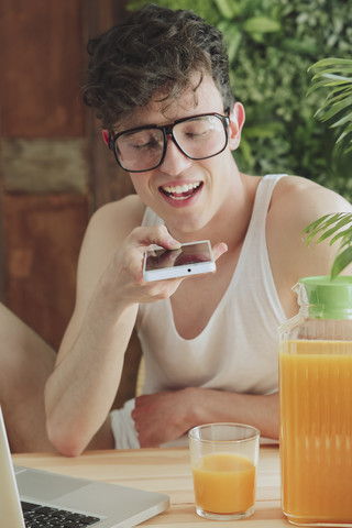 Junger Mann sendet Sprachnachricht mit Smartphone zu Hause, lizenzfreies Stockfoto