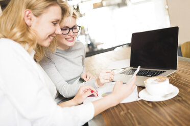 Zwei lächelnde Geschäftsfrauen arbeiten zusammen und schauen auf ihr Handy - FMOF00189