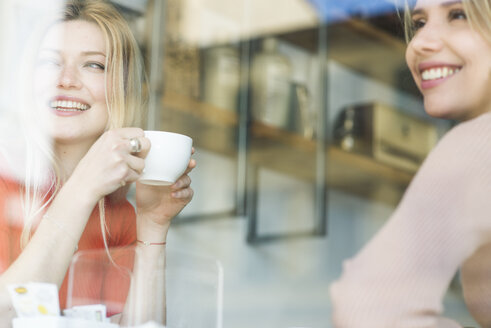 Zwei lächelnde junge Frauen in einem Cafe, die aus dem Fenster schauen - FMOF00213