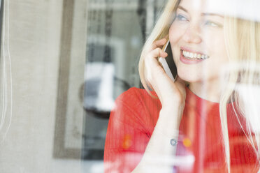 Lächelnde junge Frau am Telefon mit Blick aus dem Fenster - FMOF00214