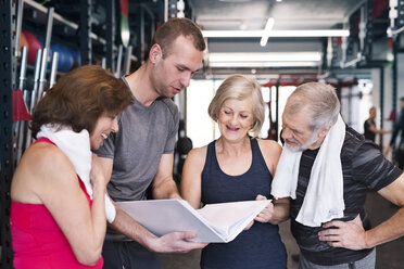 Gruppe von fitten Senioren und Personal Trainer im Fitnessstudio schauen in Ordner - HAPF01466