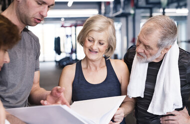 Gruppe von fitten Senioren und Personal Trainer im Fitnessstudio schauen in Ordner - HAPF01467