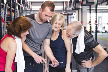 Gruppe von fitten Senioren und Personal Trainer im Fitnessstudio mit Blick auf das Tablet - HAPF01469