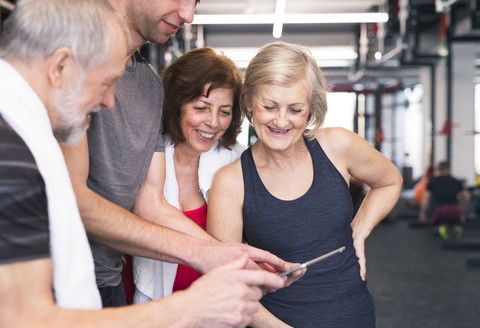 Gruppe von fitten Senioren und Personal Trainer im Fitnessstudio mit Blick auf das Tablet, lizenzfreies Stockfoto