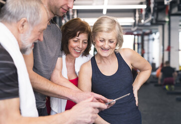 Group of fit seniors and personal trainer in gym looking at tablet - HAPF01470