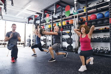 Group of fit seniors with personal trainer in gym exercising with medicine balls - HAPF01477