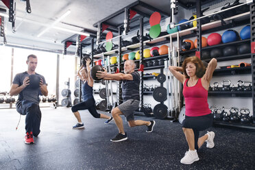 Gruppe von fitten Senioren mit Personal Trainer im Fitnessstudio beim Training mit Medizinbällen - HAPF01477