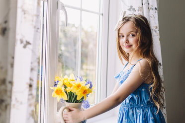 Portrait of smiling girl with flower vase of daffodils and hyacinths at home - NMSF00043
