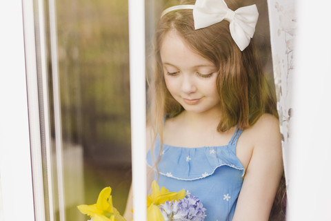 Porträt eines lächelnden Mädchens mit Schnittblumen hinter einer Fensterscheibe, lizenzfreies Stockfoto