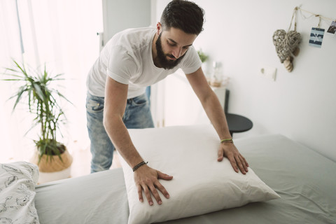 Junger Mann macht das Bett zu Hause, lizenzfreies Stockfoto