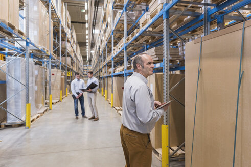 Man with tablet and two men with folder in factory warehouse - DIGF01728