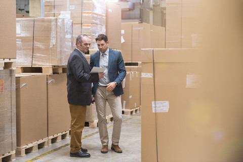 Zwei Männer betrachten ein Tablet in einem Fabriklager, lizenzfreies Stockfoto