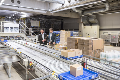 Two businessmen at conveyor belt in factory stock photo