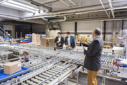 Three businessmen at conveyor belt in factory - DIGF01758