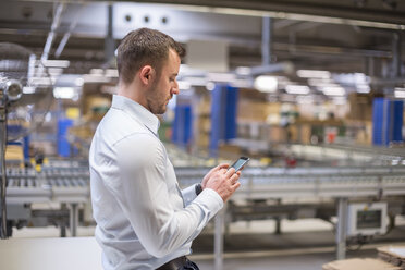 Mann in Fabrik, der auf sein Handy schaut - DIGF01767