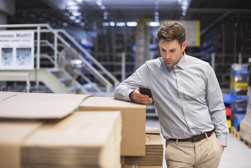 Mann in Fabrik, der auf sein Handy schaut - DIGF01770