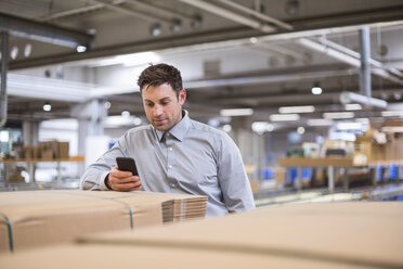 Mann in Fabrik, der auf sein Handy schaut - DIGF01771