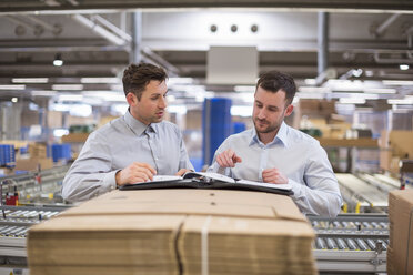 Zwei Männer in einem Fabriklager, die sich Dokumente ansehen - DIGF01773