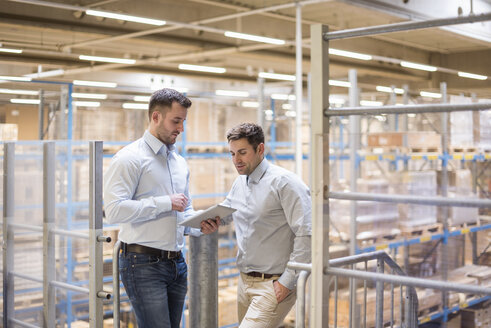 Zwei Männer in einem Fabriklager mit Blick auf ein Tablet - DIGF01775