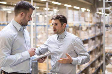 Two men with tablet talking in factory warehouse - DIGF01776